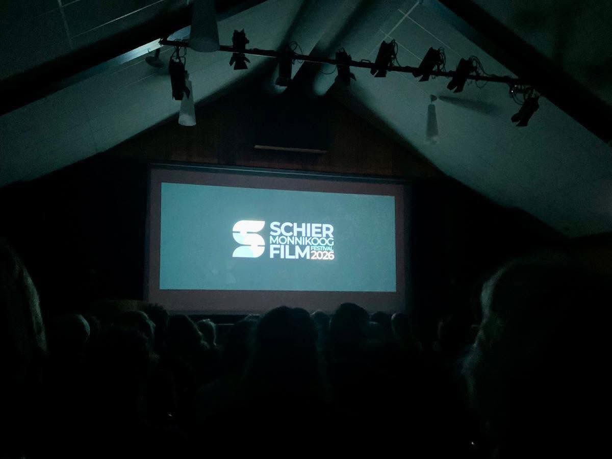 Een volle zaal in het Dorpshuis kijkt naar het filmdoek met het logo van het festival